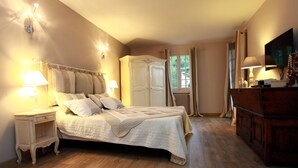 A bedroom with a large bed, bedside tables, a wardrobe, a television, and a window with curtains. - La Pelicane (Mougins)