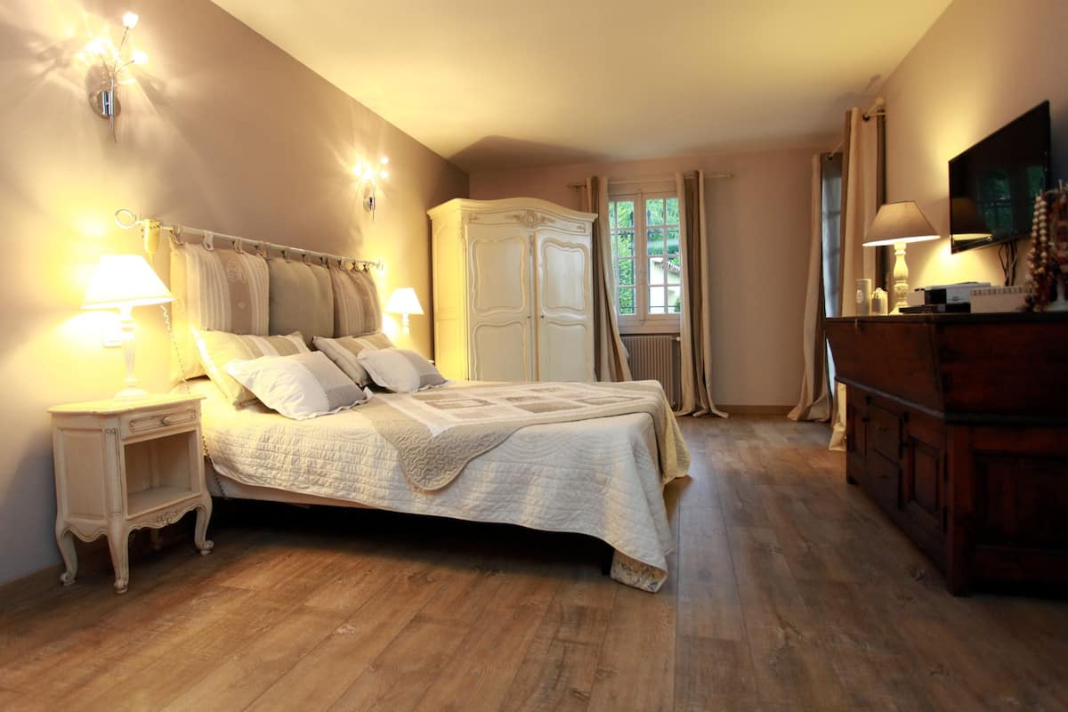 Une chambre à coucher avec un grand lit, des tables de chevet, une armoire, un téléviseur et une fenêtre avec des rideaux.