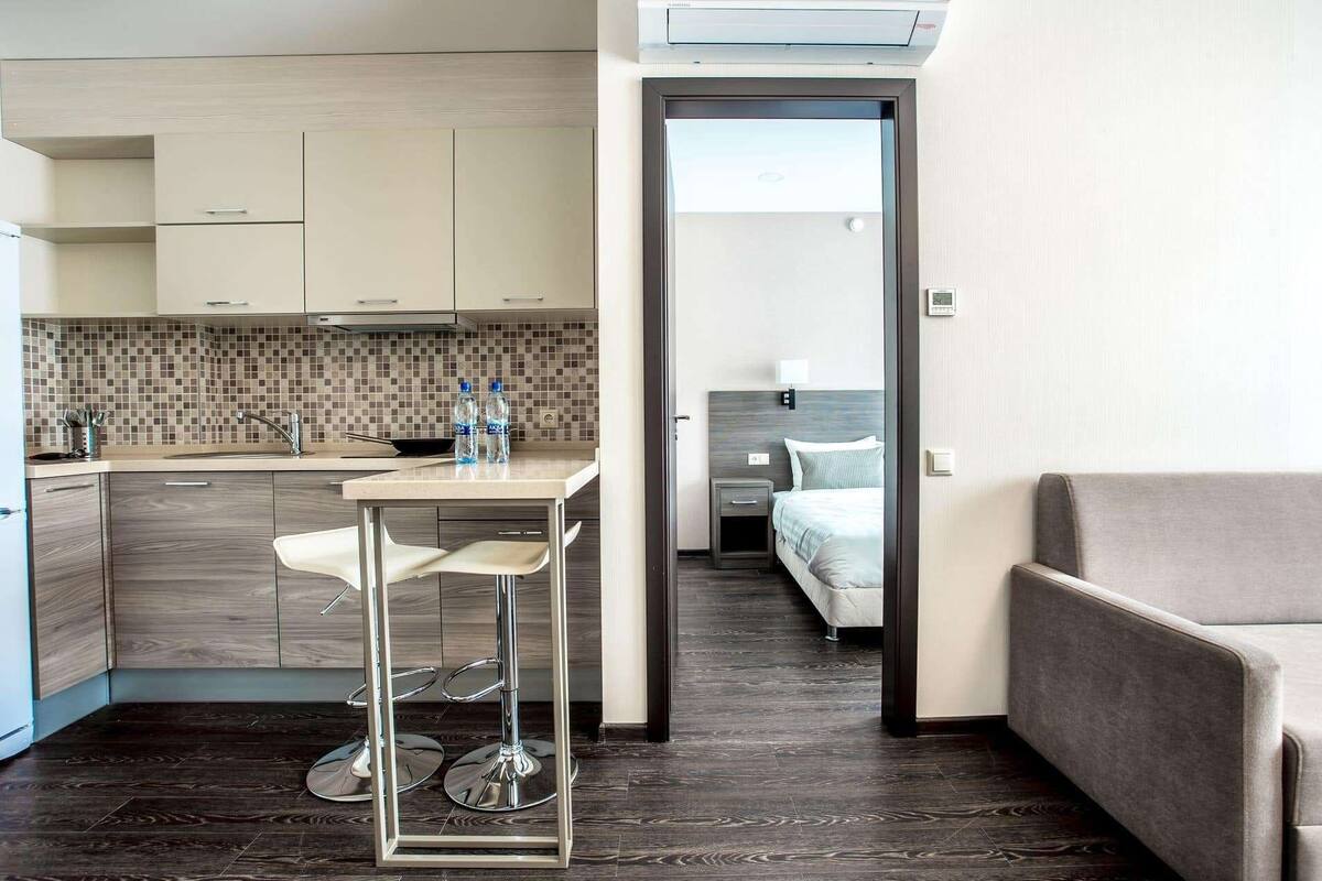 Ein kompaktes Hotelzimmer mit Küchenzeile, einem Essbereich mit Barhocker, einem Bett und einer Couch.