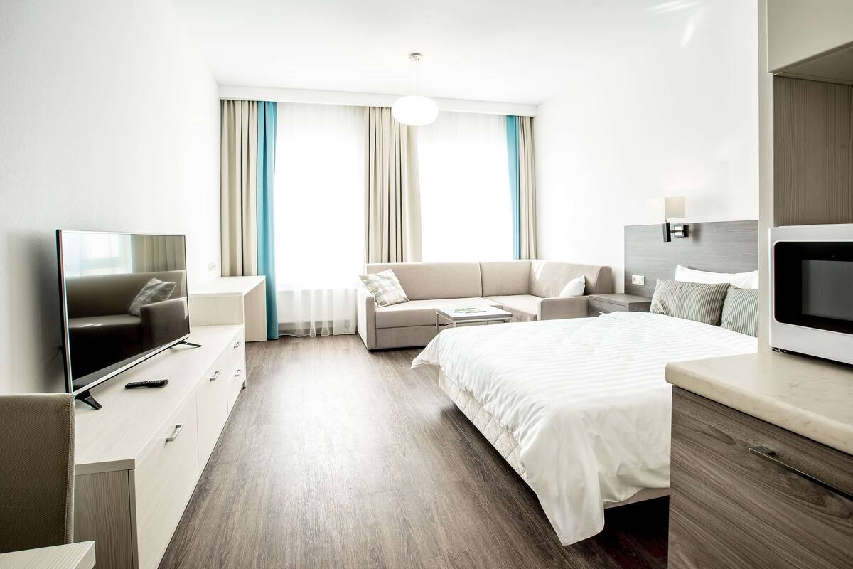 Ein modernes Hotelzimmer mit Bett, Sofa, Fernseher und Schreibtisch.