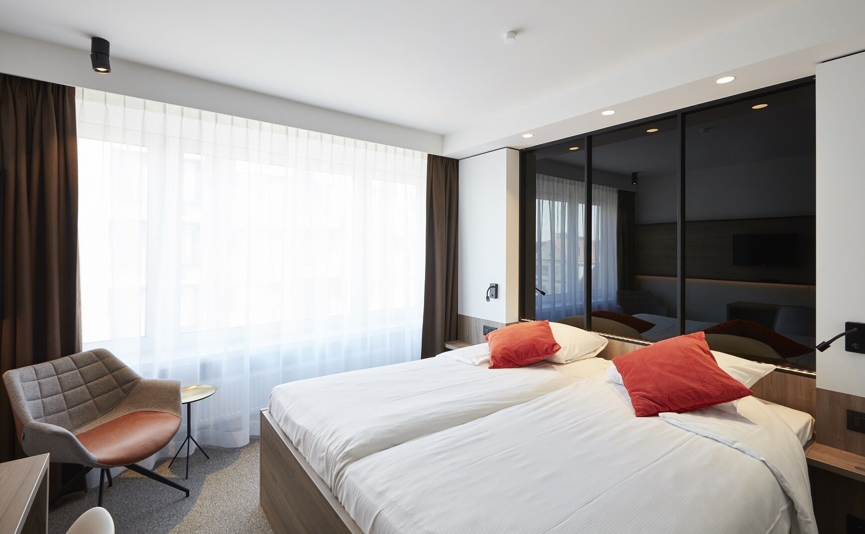 Een hotelkamer met twee bedden, een bureau, een stoel en een groot raam met gordijnen.