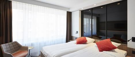 Een hotelkamer met twee bedden, een bureau, een stoel en een groot raam met gordijnen.