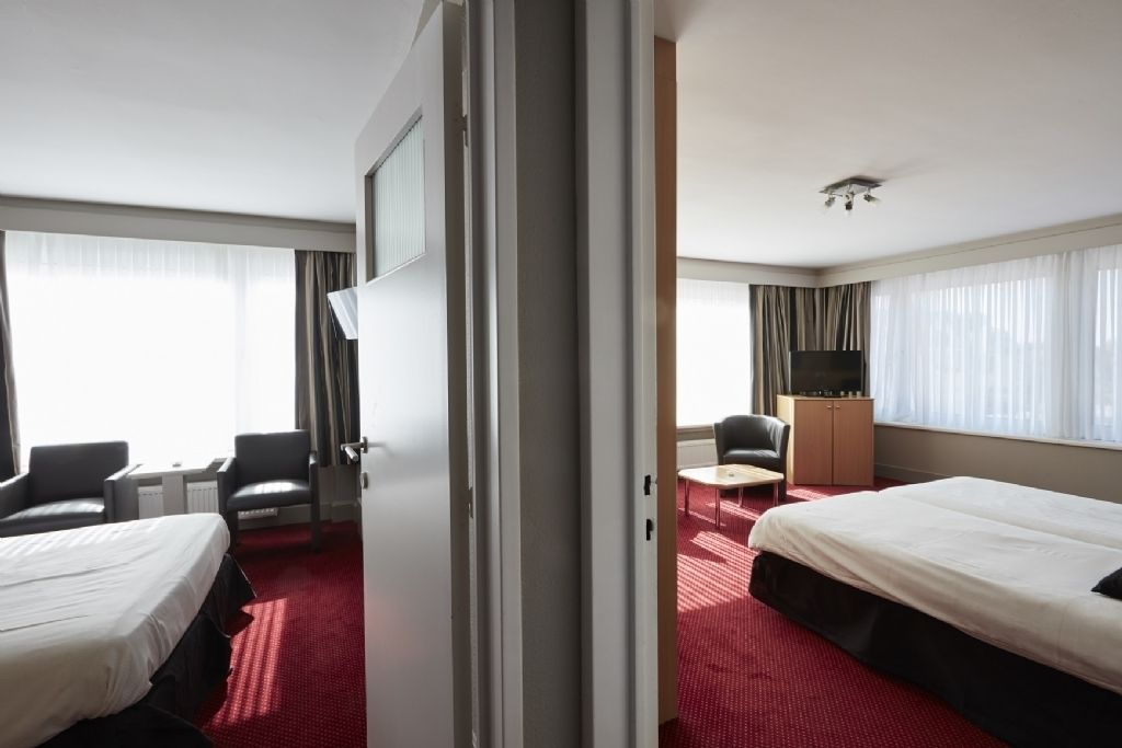 Une chambre d’hôtel avec deux lits, un bureau, une chaise, une télévision et une armoire.