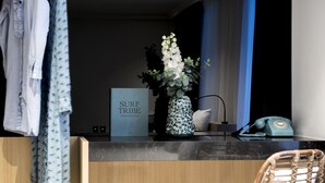 Ein Hotelrezeptionstresen mit einem Schild, auf dem "SURF TRIBE" steht, eine Vase mit Blumen, ein Telefon und ein Korbstuhl.