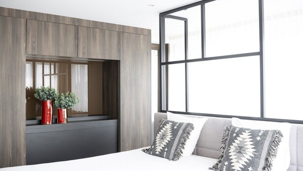 Ein modernes Schlafzimmer mit einem großen Fenster, einem Bett mit gemusterten Kissen und zwei roten Vasen mit Pflanzen.