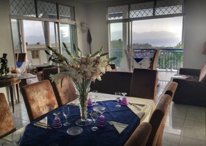 Un coin repas avec une table dressée pour quatre personnes, de grandes fenêtres offrant une vue sur la mer et un balcon doté d’une balustrade.