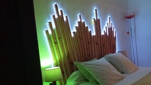 Et soveværelse med seng, puder, en sengetavlelampe, en vægmonteret lampe og en dør.