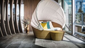 Una silla de mimbre con dosel, una planta en maceta y vista de edificios a través de una ventana.