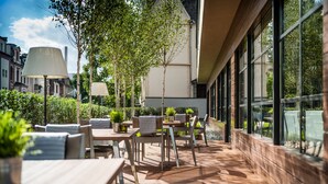 Un patio al aire libre con mesas y sillas de madera, plantas en macetas y un farol.