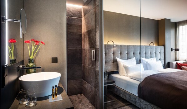 Une chambre d’hôtel moderne dotée d’un grand lit, d’une salle de bain avec baignoire et d’une coiffeuse avec un lavabo et un miroir.