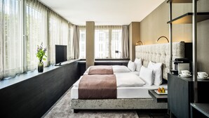 Habitación de hotel moderna con una cama grande, televisión, cafetera y vista a la ciudad.