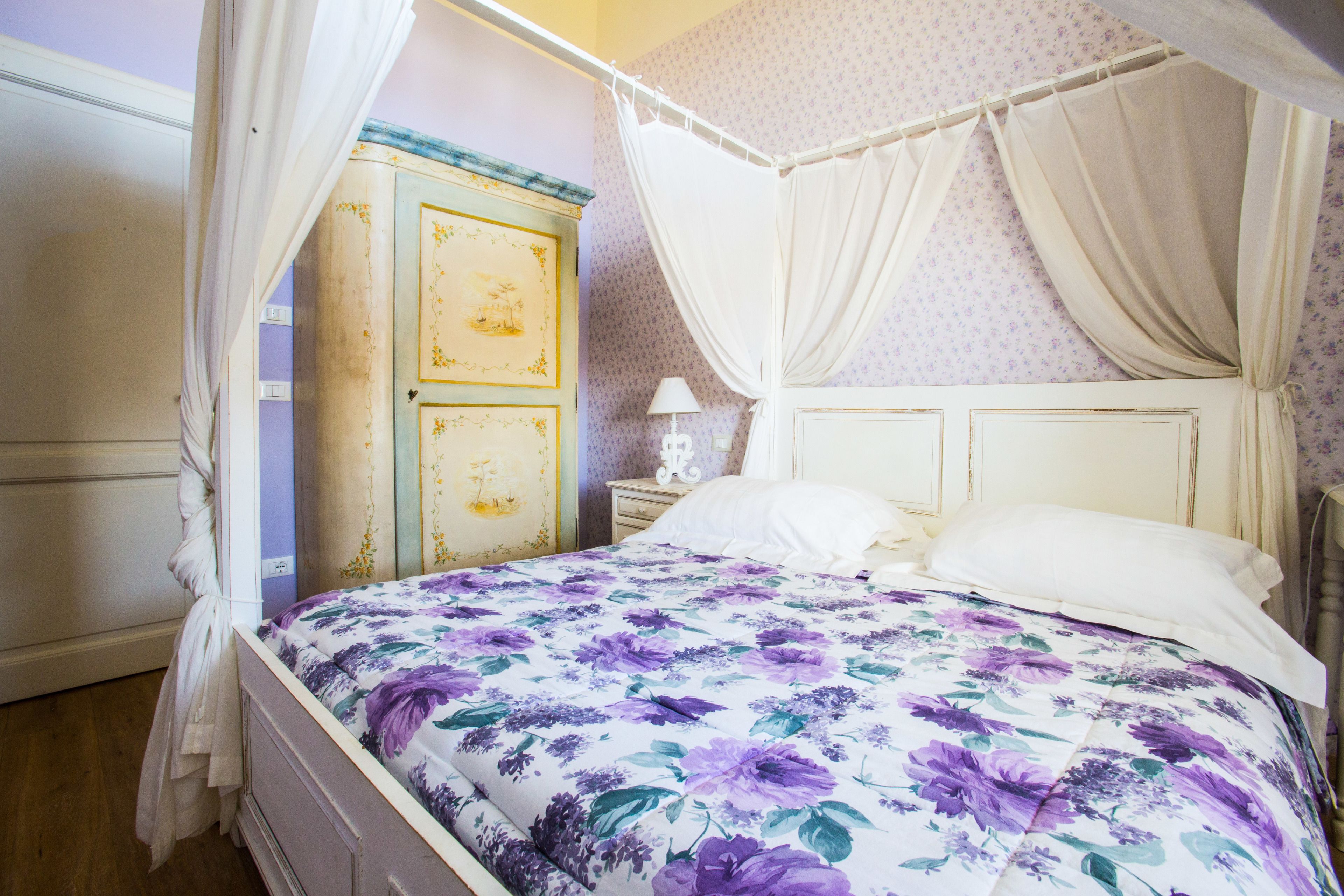 A bedroom with a four-poster bed, a nightstand with a lamp, and a wardrobe.