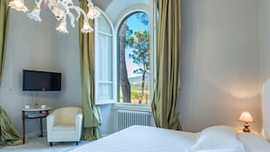 Een hotelkamer met een bed, een stoel, een televisie, een lamp en een raam met gordijnen.