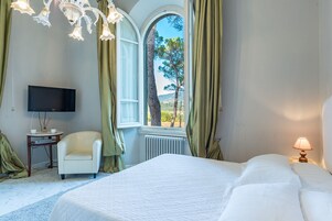 Una habitación de hotel con cama, una silla, televisión, lámpara y ventana con cortinas.
