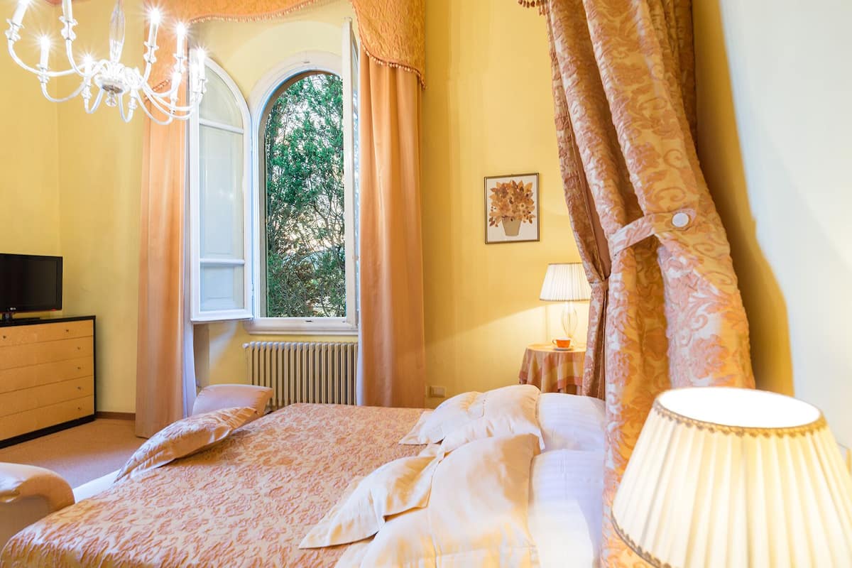Une chambre à coucher avec un lit, une commode, une fenêtre avec des rideaux, un lustre et une lampe.