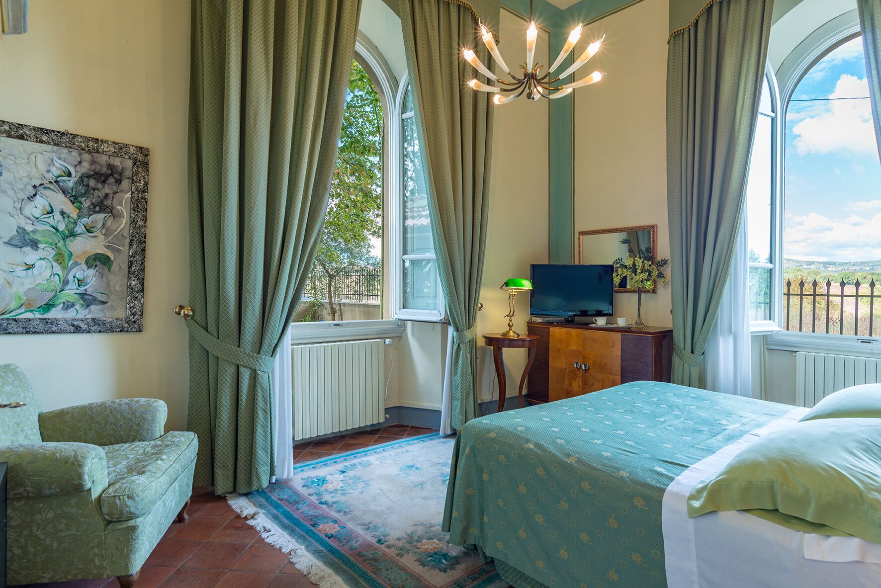 A bedroom with a bed, a desk with a TV, a chair, and a painting on the wall.