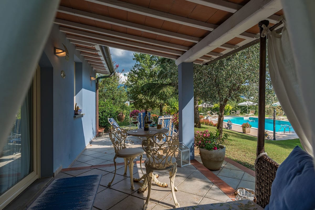 Un patio couvert avec une table et des chaises, une vue sur une piscine et un espace jardin.