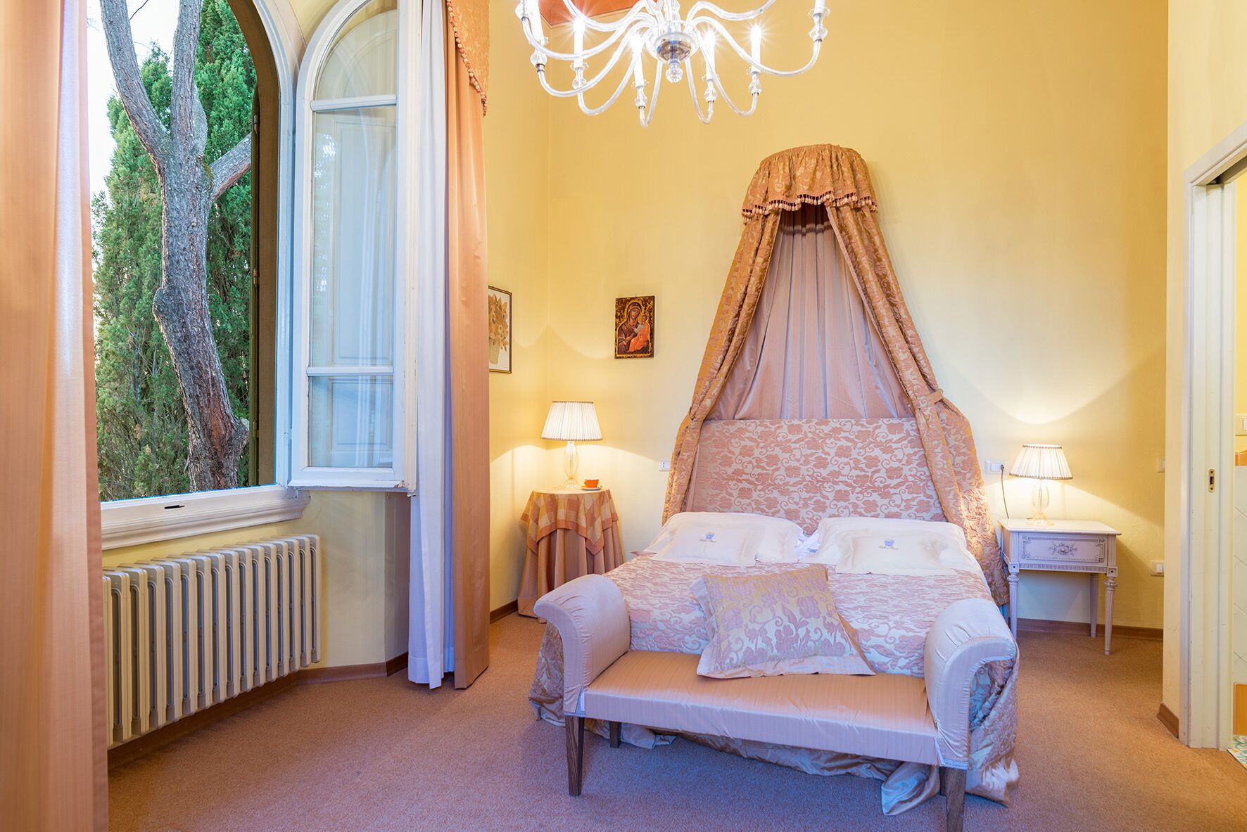 Une chambre à coucher avec un grand lit, une fenêtre avec des rideaux, un radiateur et un lustre.