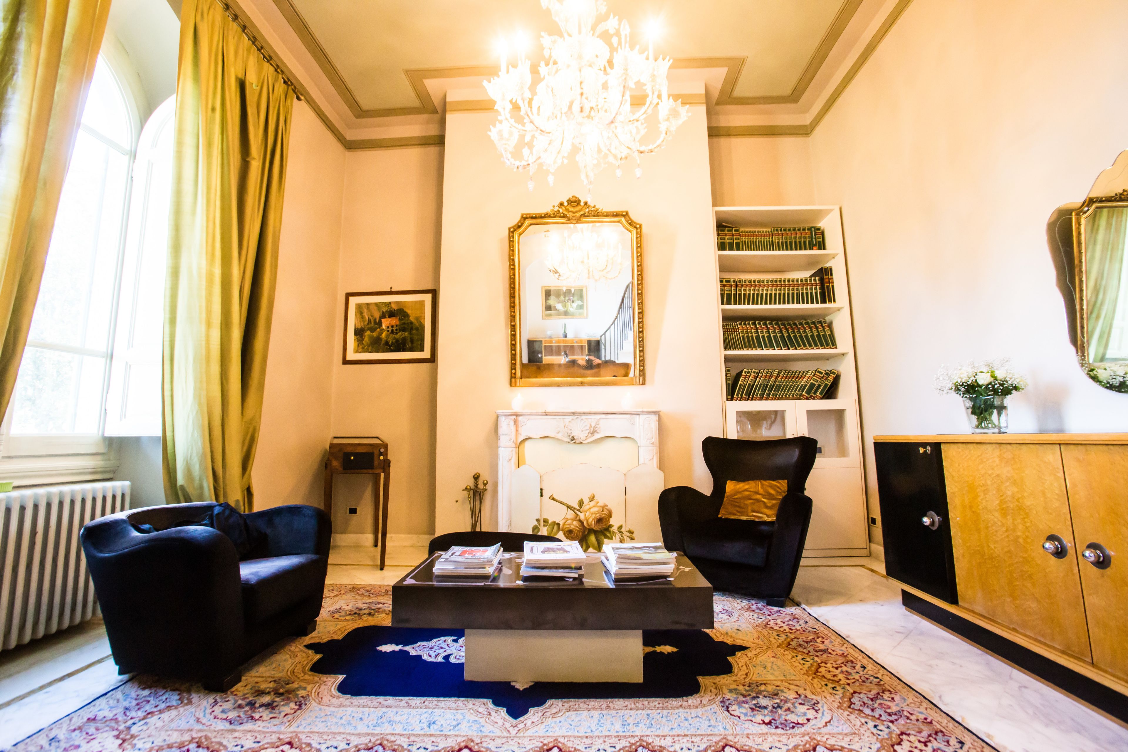 Una sala de estar con chimenea, candelabro, estantería y un espejo grande.