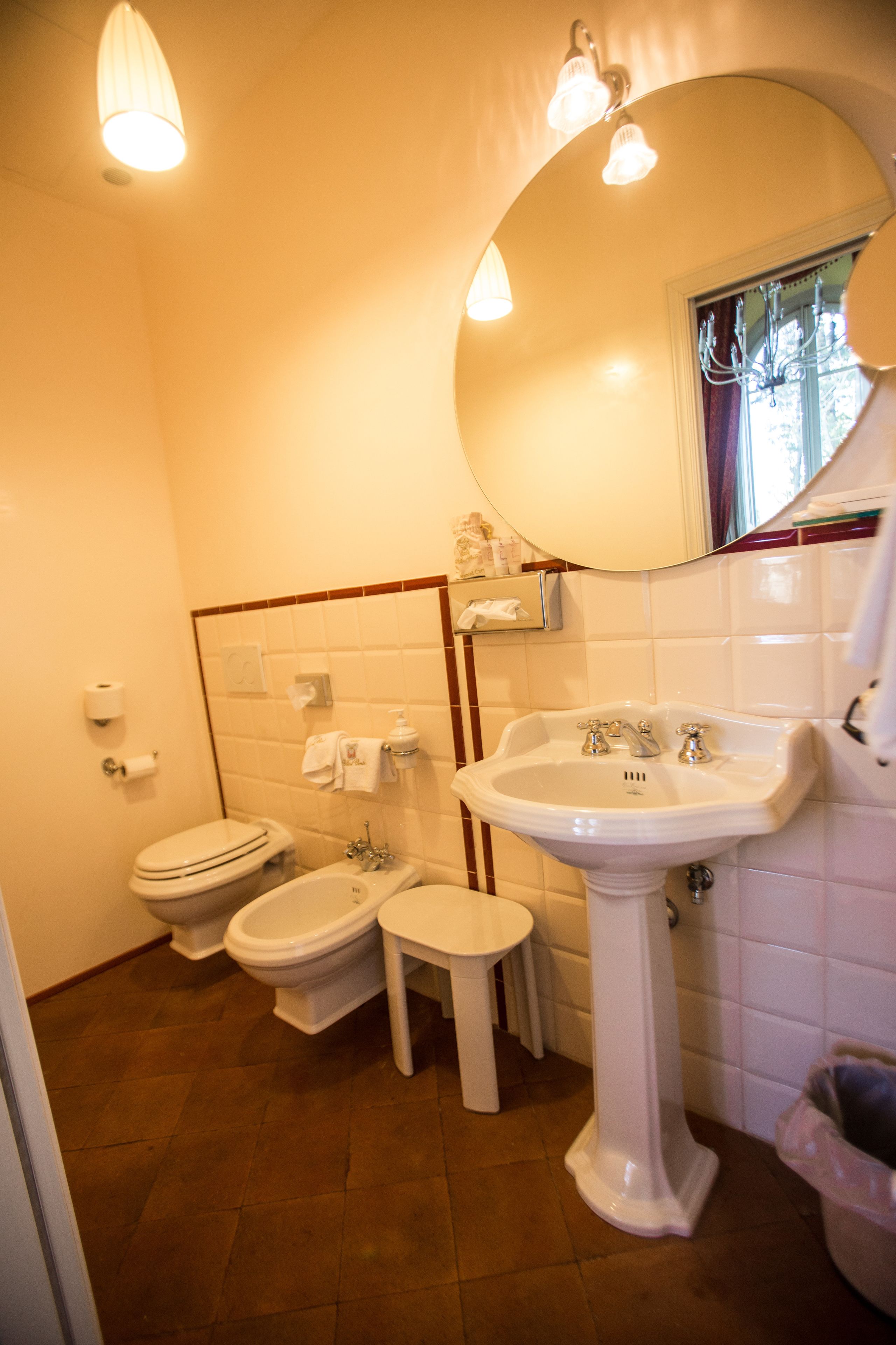 Ein Badezimmer mit einem Standwaschbecken, zwei Toiletten, einem Spiegel und einem Handtuchhalter.