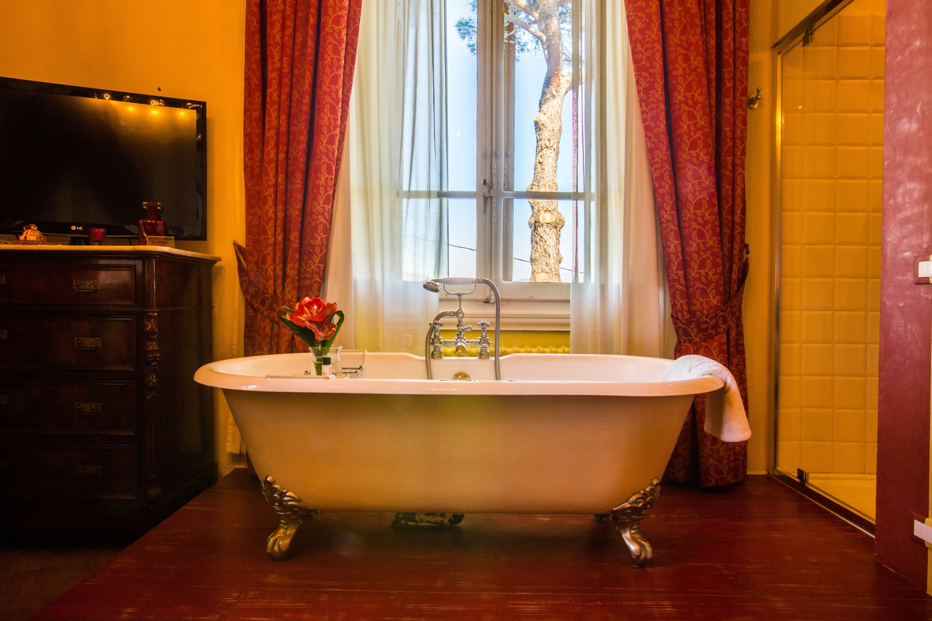 Un baño con una bañera de patas de león, un mueble de madera, un espejo y una ventana con cortinas.