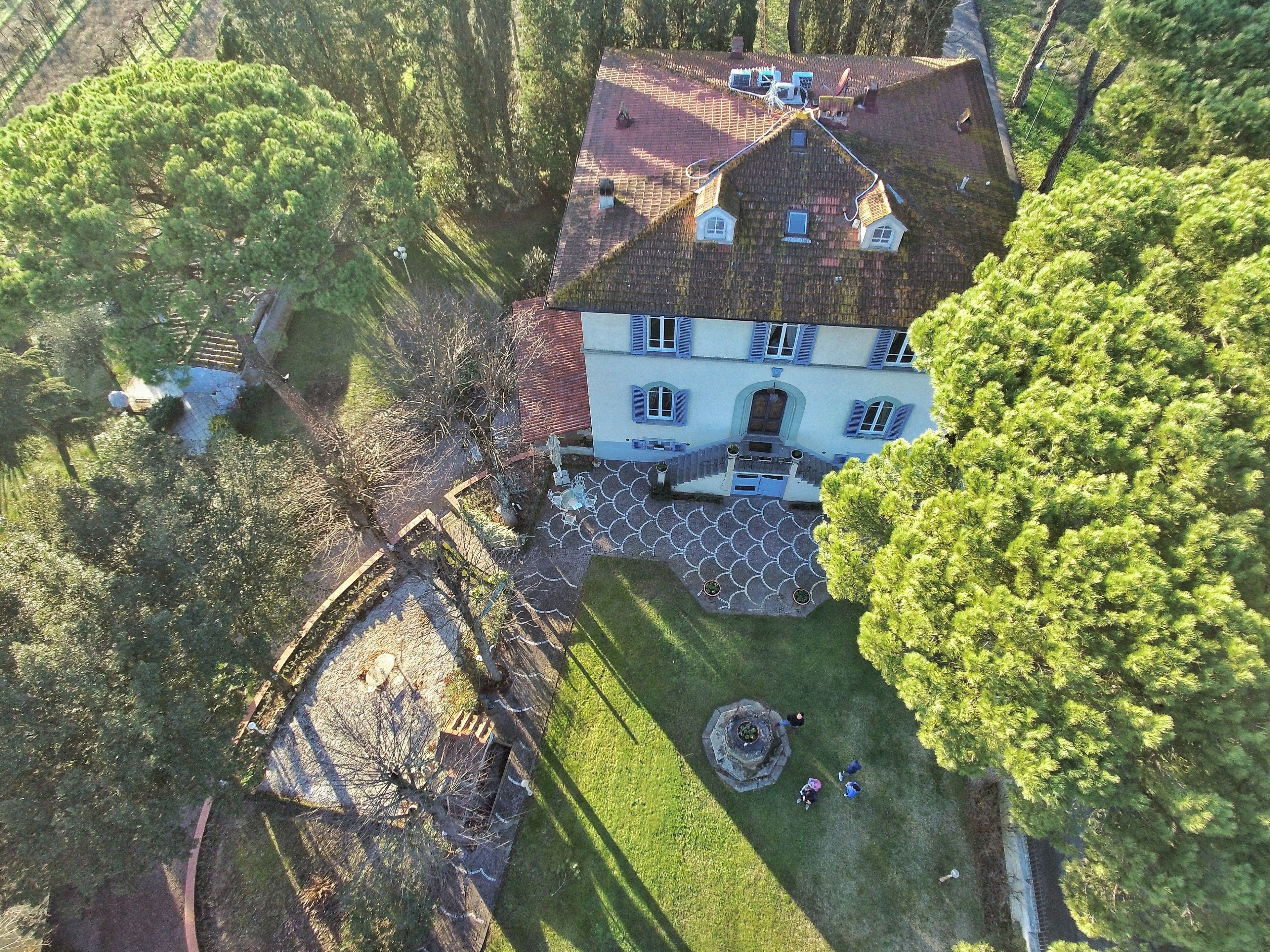Une vue aérienne d’une grande maison dotée d’une cour spacieuse, d’un jardin bien entretenu et d’une fontaine centrale.