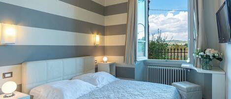 A hotel room with a bed, bedside lamps, a window with a view, and a radiator.