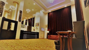 A hotel lobby with a reception desk, a red sofa, a small table, and a patterned carpet. - Treasures Suites & Conferences (Abuja)