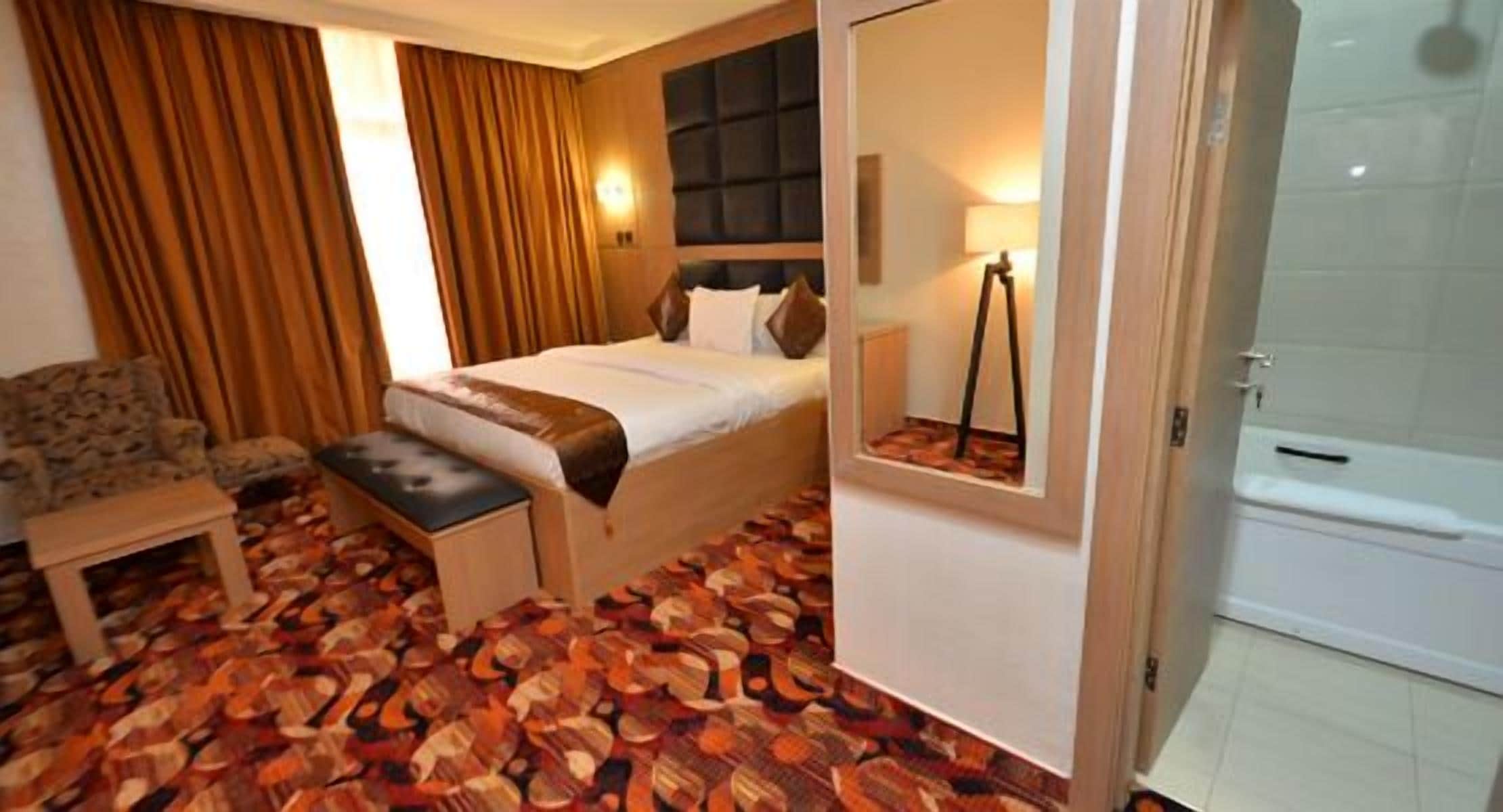A hotel room with a bed, a small table, a chair, a window with curtains, and a bathroom.