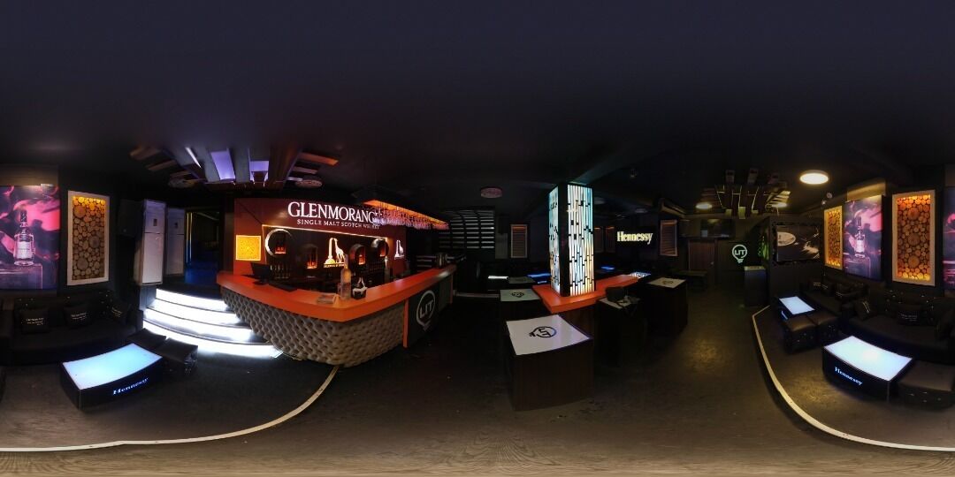 A bar area with a neon sign for Glenmorangie whisky, a modern bar counter, and a seating area with tables and chairs.