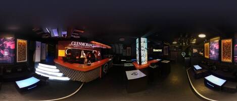 A bar area with a neon sign for Glenmorangie whisky, a modern bar counter, and a seating area with tables and chairs.
