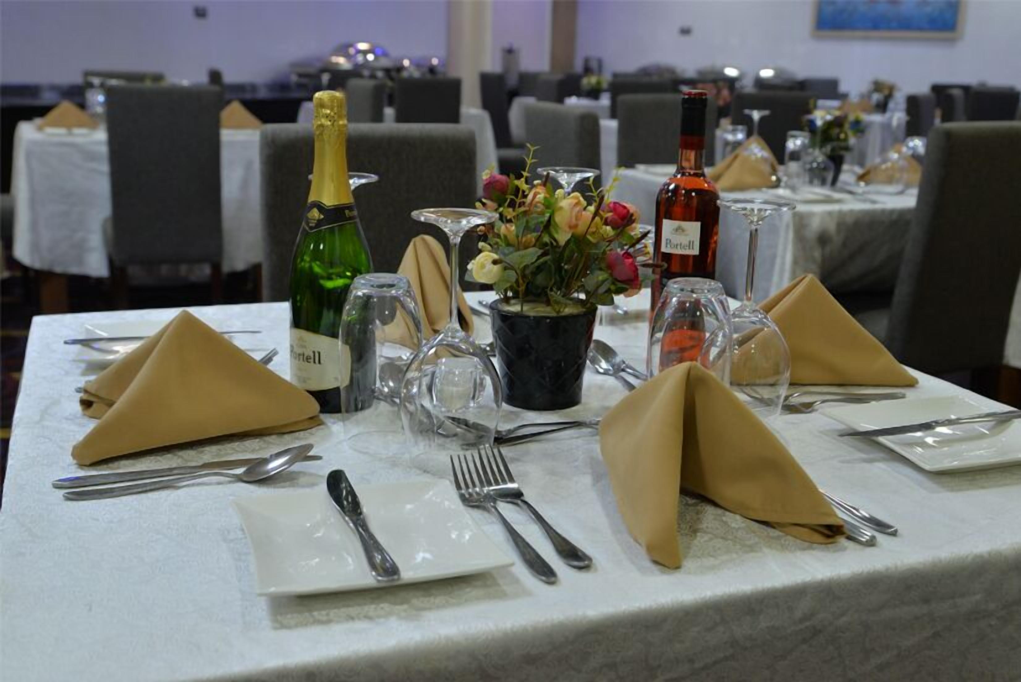 A dining table set with a bottle of Port wine, a vase with flowers, and a bottle of rosé wine.