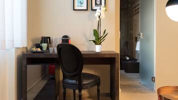 A modern room with a desk, a chair, a coffee maker, a potted orchid, and framed pictures on the wall.