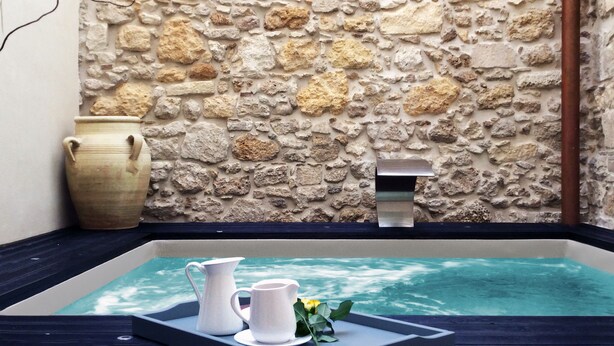 A stone wall with a small pool, two white pitchers, and a vase. - CinqueSuites Ortigia (Syracuse)