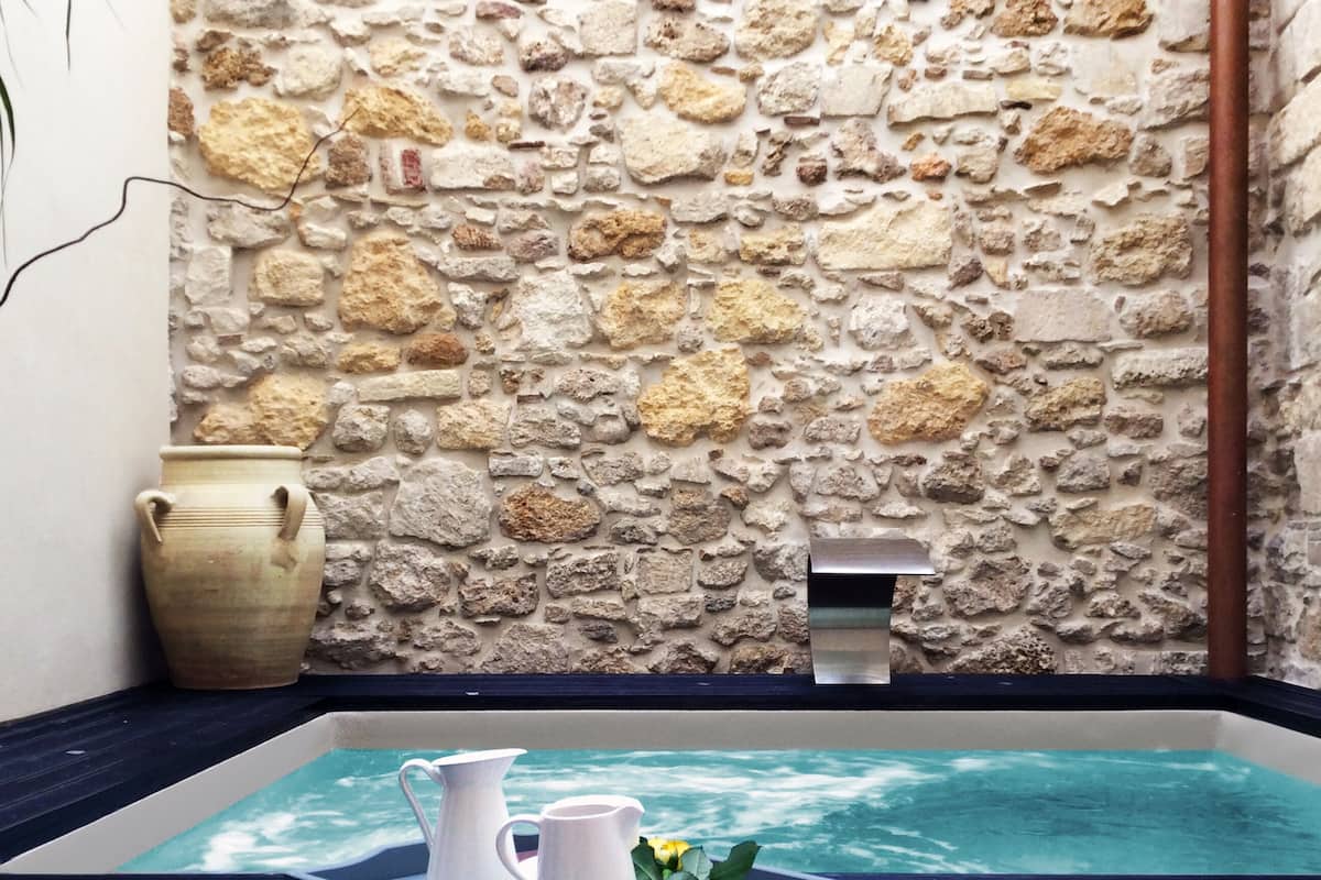 A stone wall with a small pool, two white pitchers, and a vase.