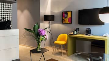 Ein modernes Wohnzimmer mit einem gelben Sessel, einer schwarzen Stehlampe, einem Glastisch und einem flachbildfernseher, der an der Wand montiert ist.