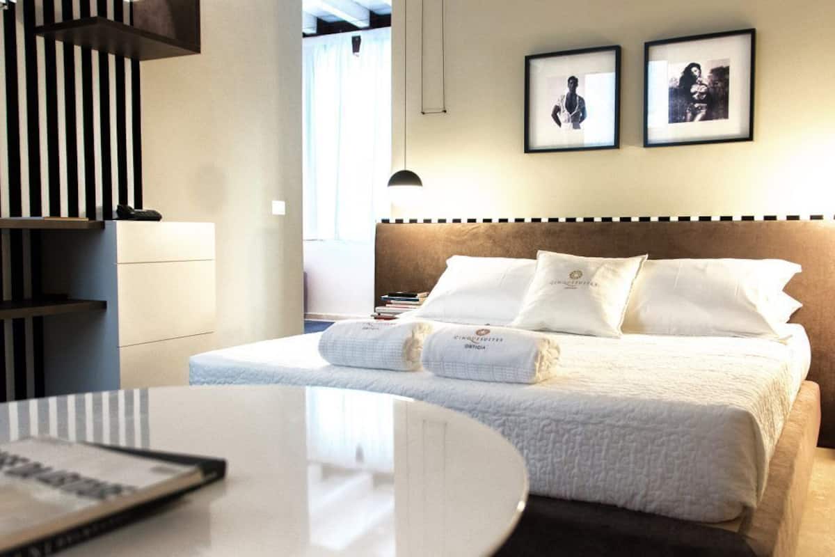 A hotel room with a bed, bedside tables, a desk, and a bookshelf.