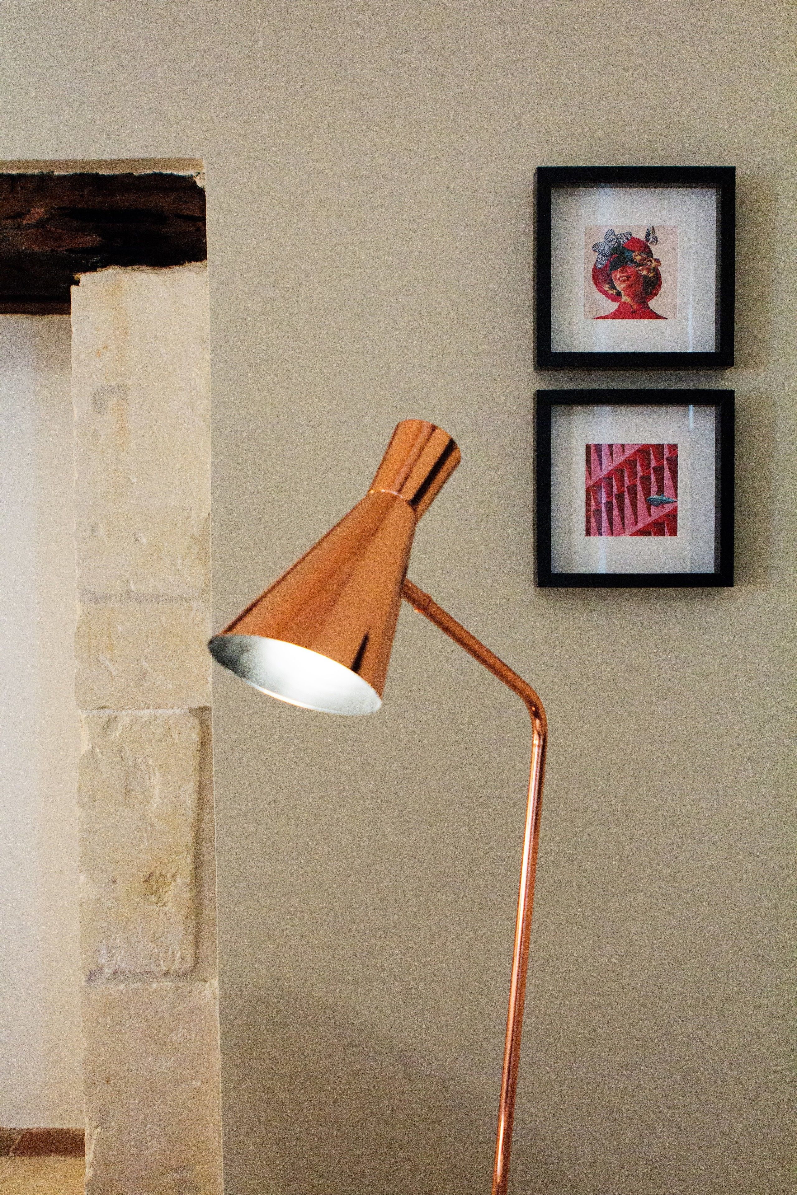 A copper desk lamp in a room with a brick wall and two framed pictures on the wall.