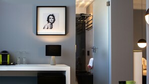 A modern bathroom with a framed picture, a sink with glassware, a towel rack, and a small table with a cup. - CinqueSuites Ortigia (Syracuse)