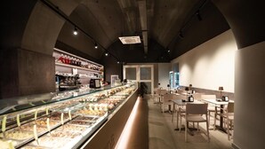 A restaurant with a long counter, glass display case with food, and seating area. - CinqueSuites Ortigia (Syracuse)