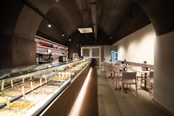Un restaurante con una barra larga, vitrina de vidrio con comida y zona de mesas.