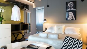 A modern hotel room with a bed, a desk, and a chair. There are towels on the bed and a plant on the desk. - CinqueSuites Ortigia (Syracuse)