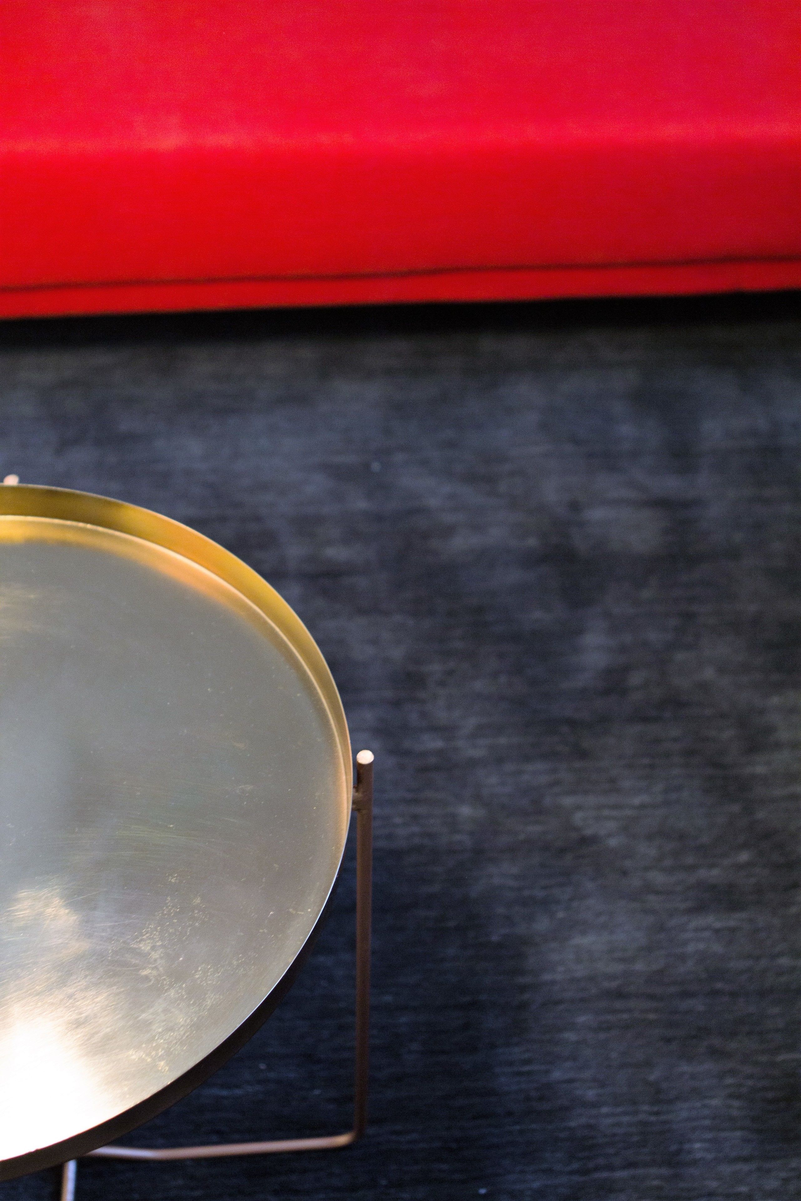 Una mesa redonda metálica con superficie reflectante, sobre una base oscura y un fondo rojo.