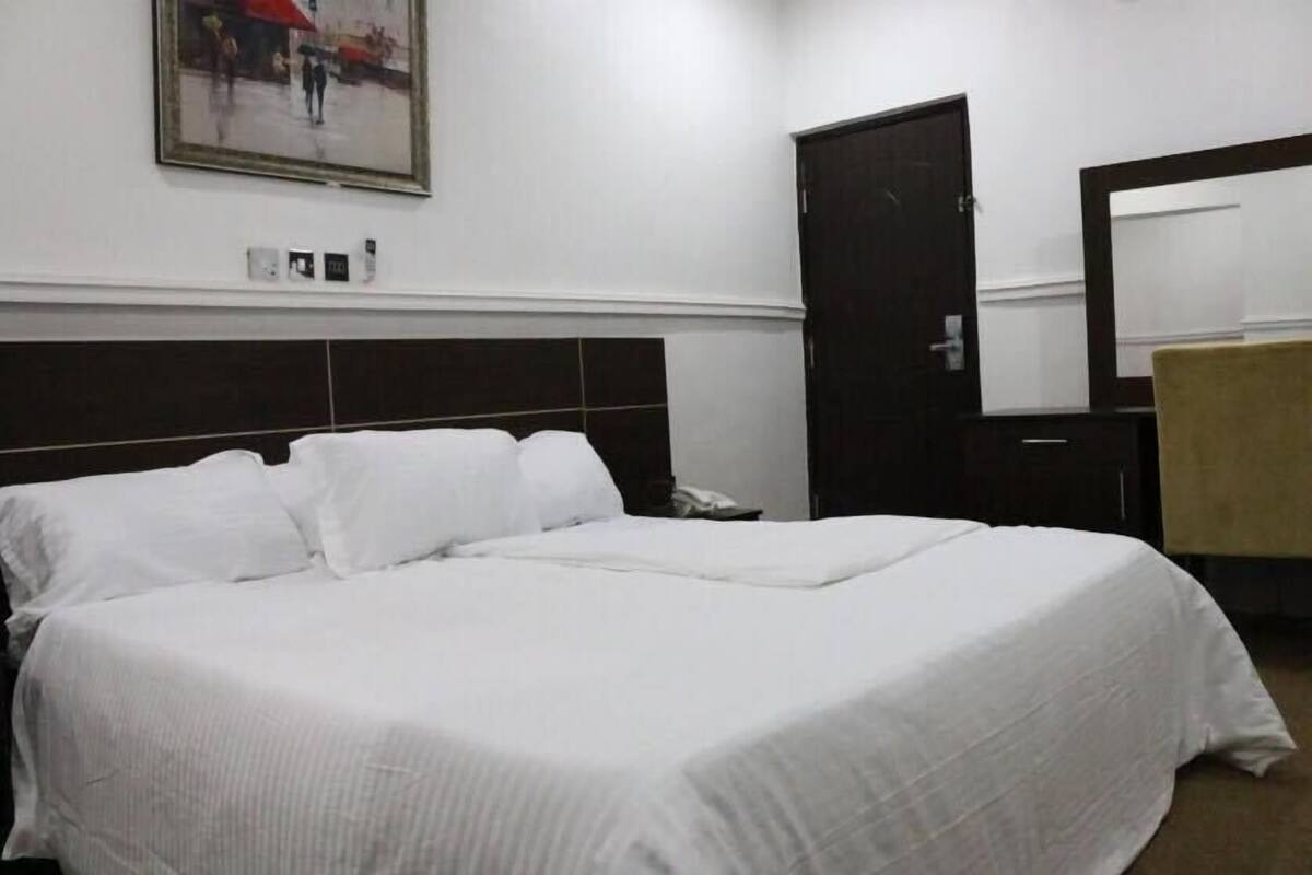 Une chambre d’hôtel avec un grand lit, une tête de lit en bois foncé, une porte, un miroir et un tableau encadré au mur.