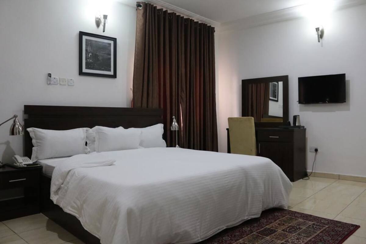 Une chambre d’hôtel avec un lit, une table de chevet, une lampe, une télévision et un miroir.