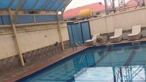 An indoor swimming pool with clear blue water, surrounded by a covered area with a metal roof structure. - The Den Hotel (Abuja)