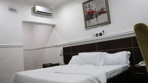 A hotel room with a bed, a nightstand, a telephone, and a painting on the wall. - The Den Hotel (Abuja)