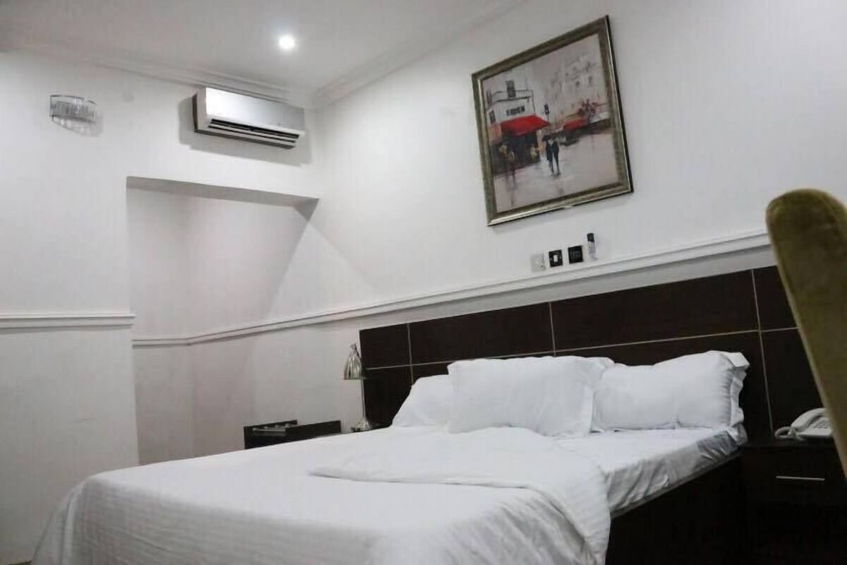Une chambre d’hôtel avec un lit, une table de chevet, un téléphone et un tableau au mur.