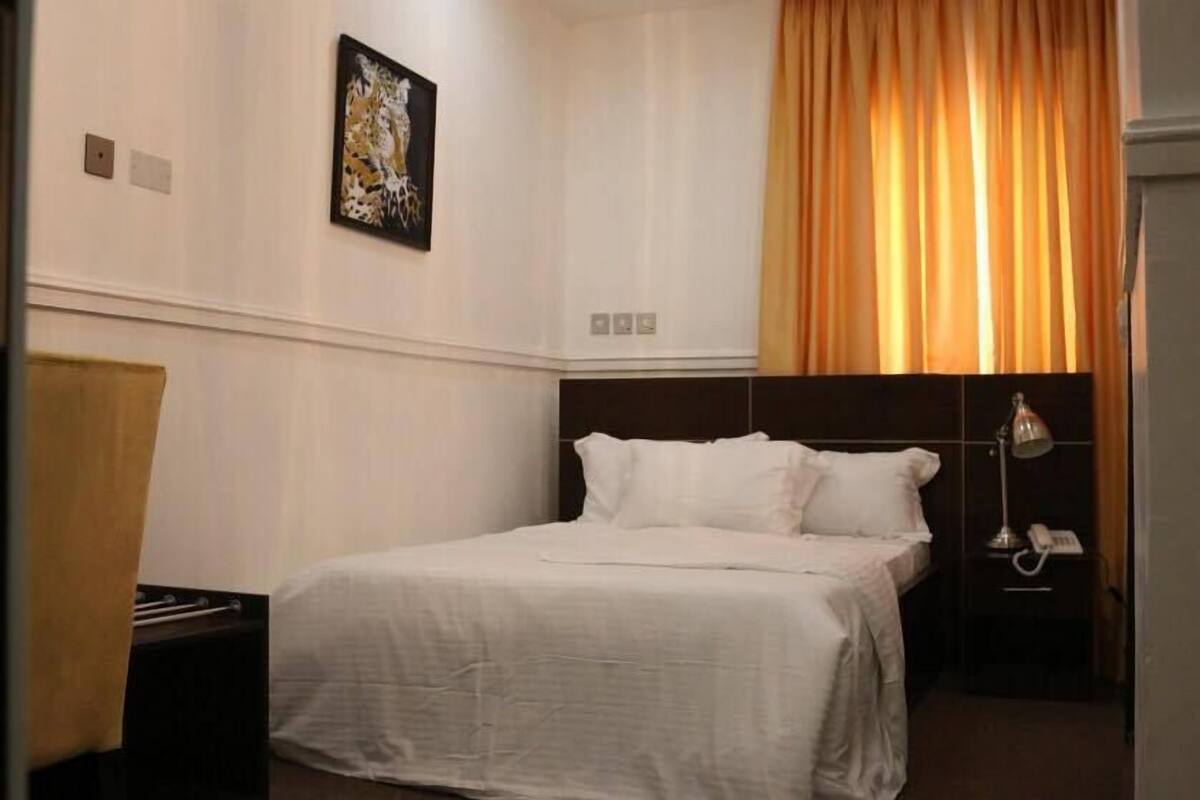 Une chambre d’hôtel avec un lit, un bureau, une lampe et un tableau au mur.