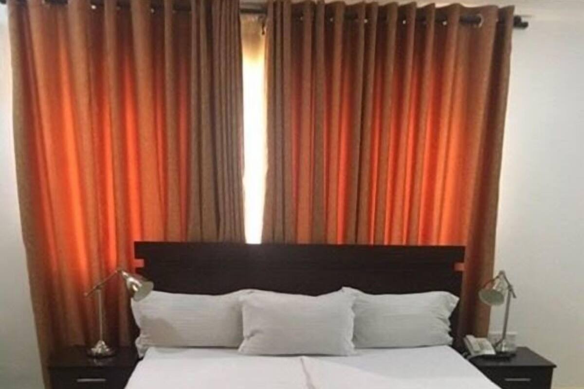 Un lit bien fait, avec du linge de lit blanc, deux tables de chevet avec des lampes et un tapis à motifs sur un sol carrelé.